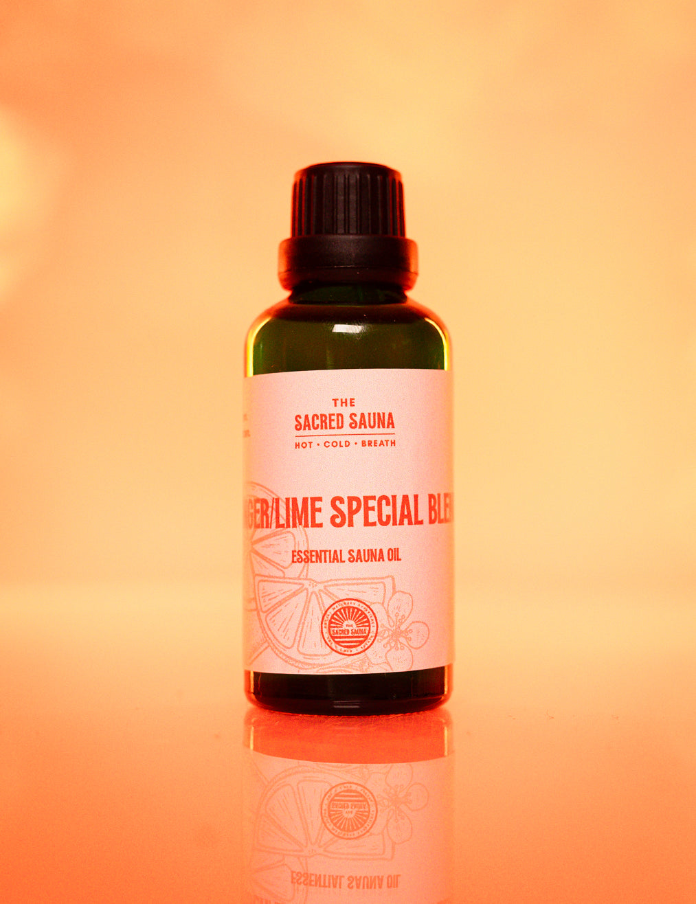 Lime Special Blend' eterisk olja från The Sacred Sauna, stående på en reflekterande yta med mjuk orange bakgrund. Flaskan är designad för användning i bastu och ger en uppfriskande doft av ingefära och lime.