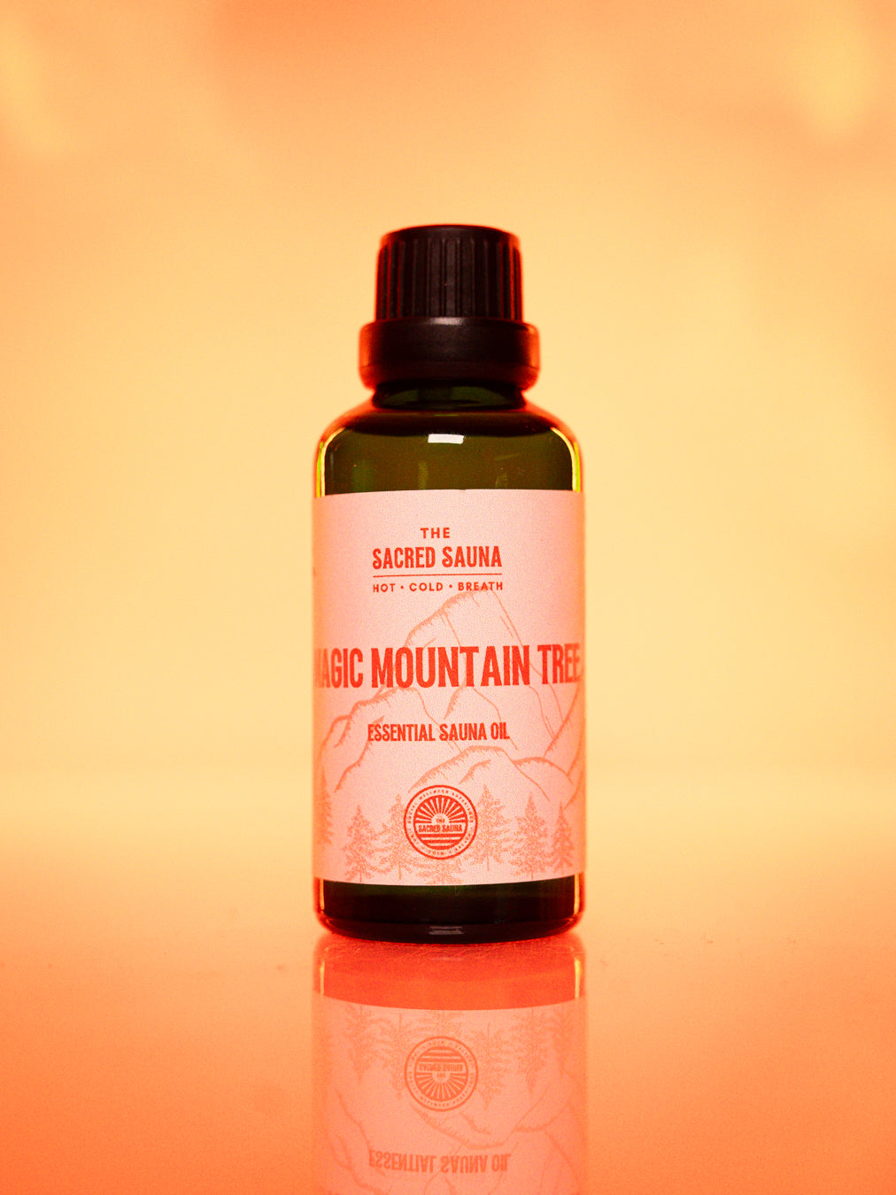 Flaska med 'Magic Mountain Tree' eterisk olja från The Sacred Sauna, stående på en reflekterande yta med mjuk orange bakgrund. Flaskan är designad för användning i bastu och ger en uppfriskande doft av skog och natur.